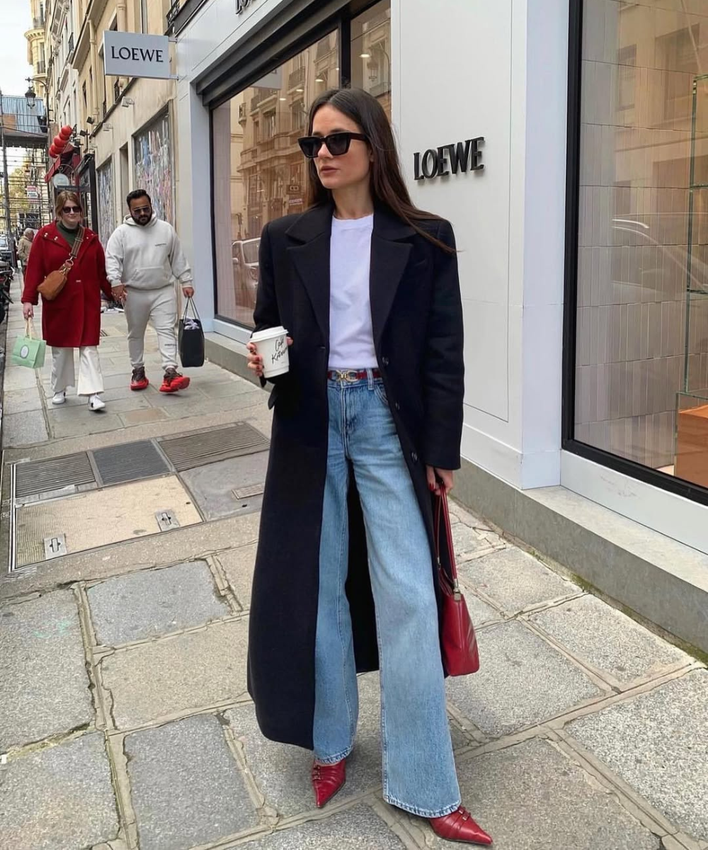 Looks com scarpin: modelo posa com casaco preto, jeans amplo e scarpin vermelho diante da LOEWE. Texto: LOEWE