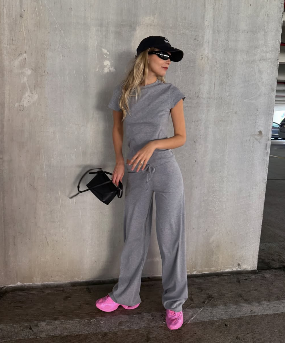 Looks com calça de moletom: modelo posa com conjunto cinza amplo, boné preto, bolsa preta e tênis rosa em clima urbano