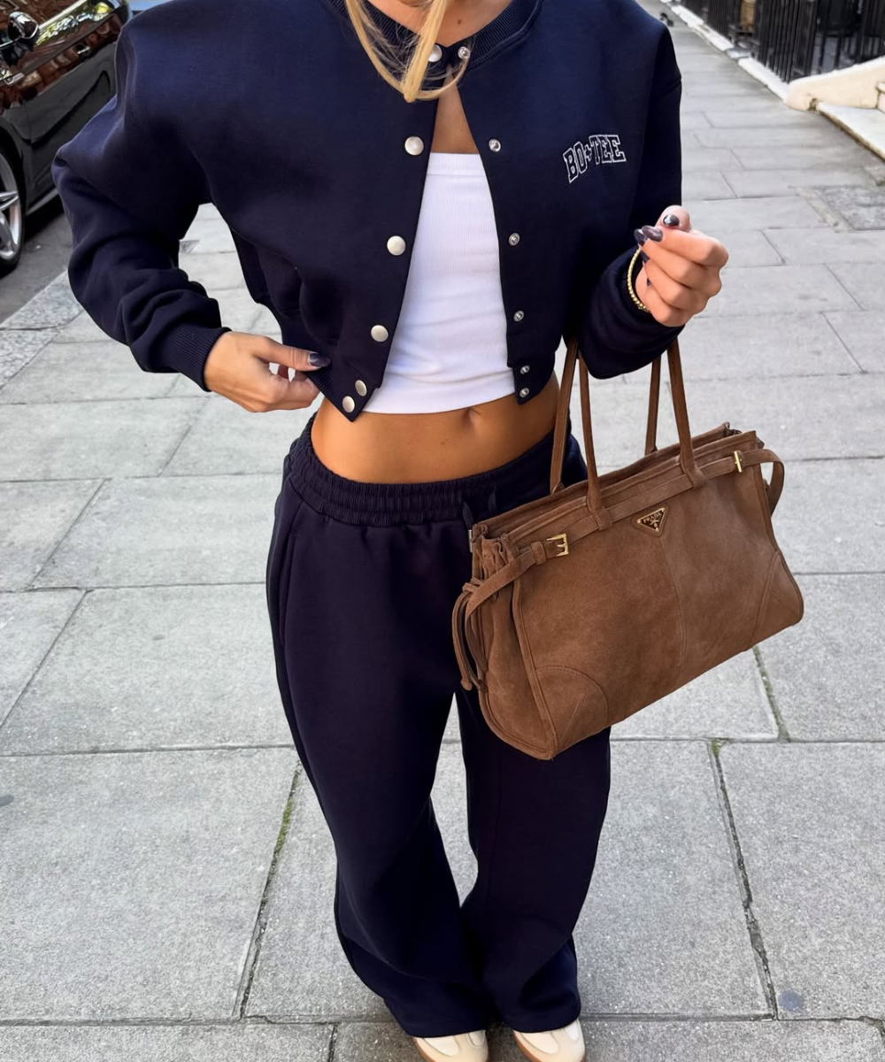 Looks com calça de moletom: modelo posa com jaqueta college marinho, top branco e bolsa marrom. Texto: BOOTEE