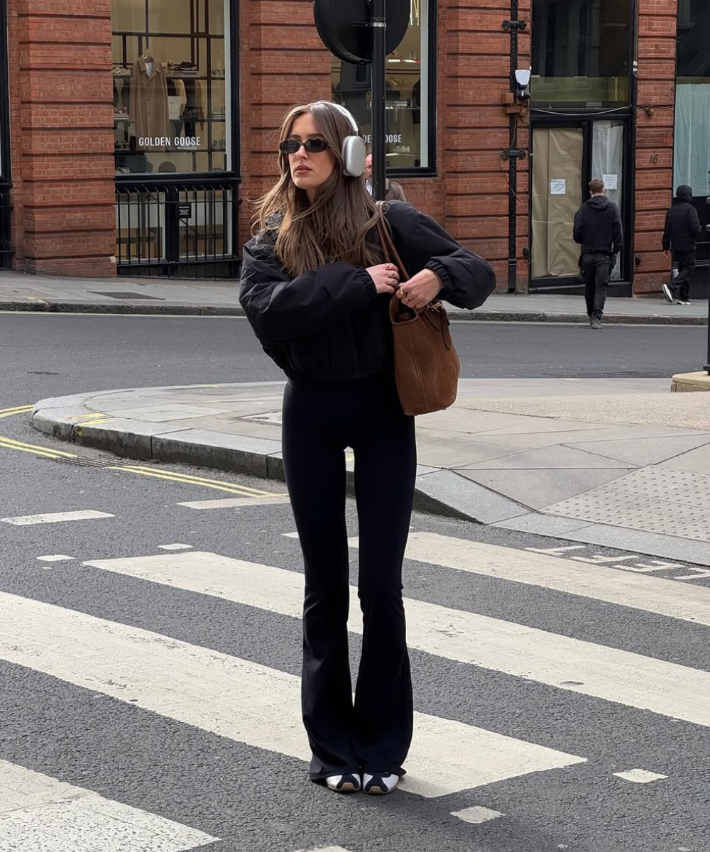 Looks com calça de moletom preta flare e jaqueta oversized; modelo posa na faixa com bolsa marrom.