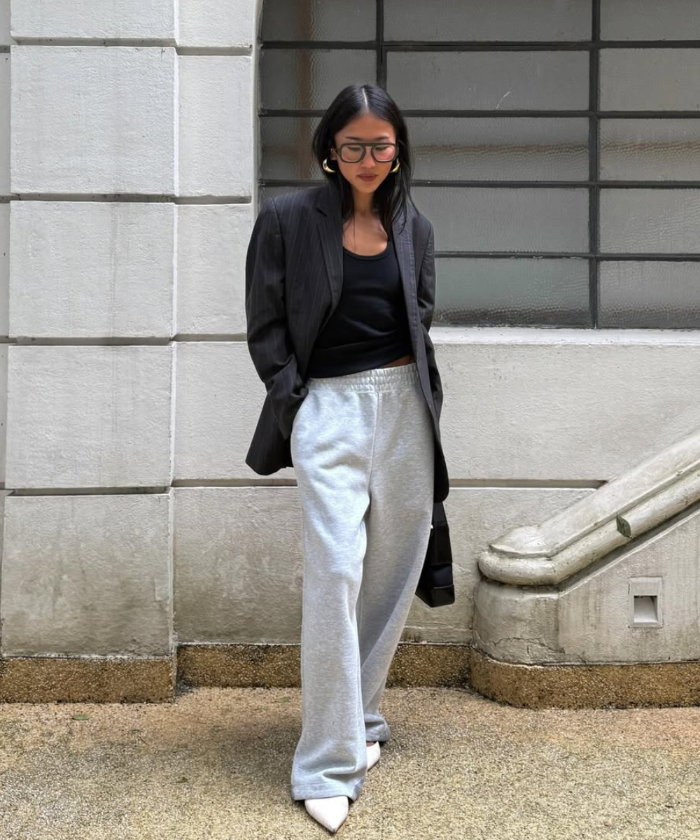 Looks com calça de moletom cinza e caimento reto ganham blazer preto; modelo posa com elegância urbana serena.