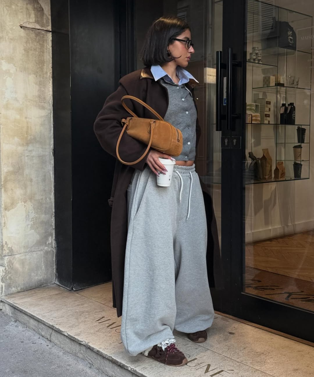 Looks com calça de moletom cinza ampla: modelo posa com casaco marrom, camisa azul e bolsa caramelo em clima urbano casual.