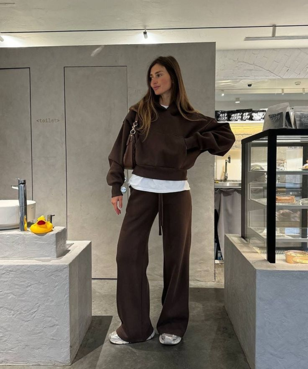 Looks com calça de moletom marrom ampla e hoodie cropped; modelo posa com estilo casual em café minimalista.