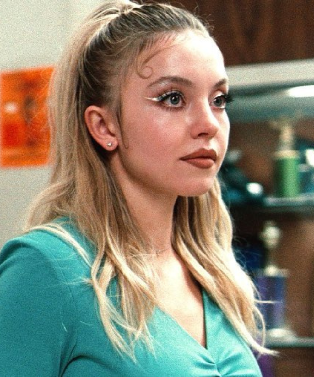 Maquiagens de euphoria em destaque: modelo posa com delineado branco gráfico, brilho suave e blusa verde, em clima intenso.