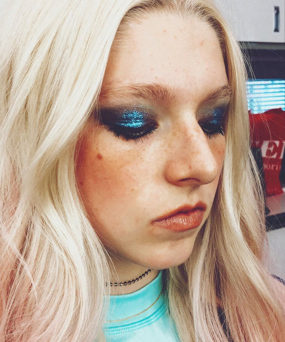 Maquiagens de euphoria em modelo de perfil, sombra azul com glitter, cabelo platinado e clima dramático e cool