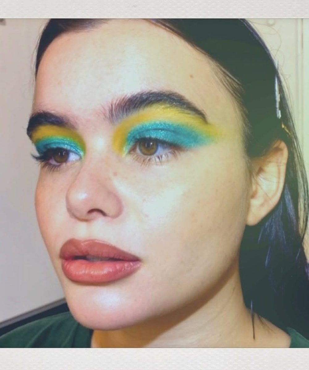 Modelo posa com maquiagens de euphoria em sombra azul turquesa e amarela vibrante, brilho intenso e clima ousado.