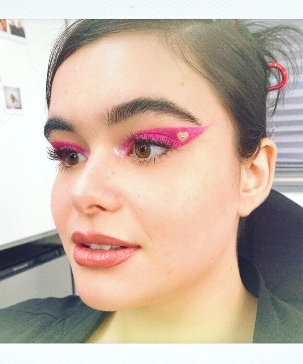 Modelo posa com maquiagens de euphoria em rosa neon cintilante, delineado gráfico e strass, clima ousado e pop.