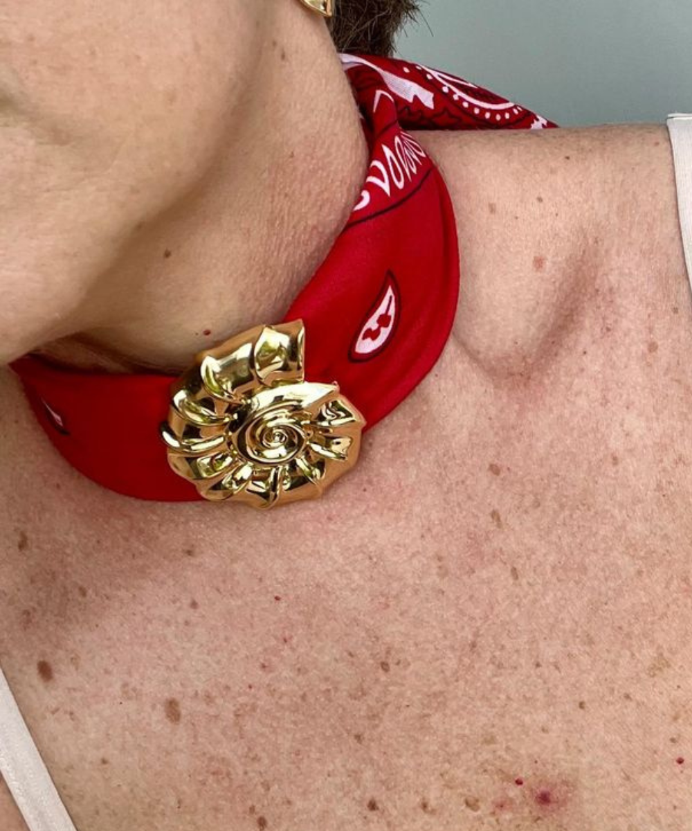 Lenço com pingente dourado em flor envolve o pescoço com estampa vermelha e branca, destacando estilo marcante.