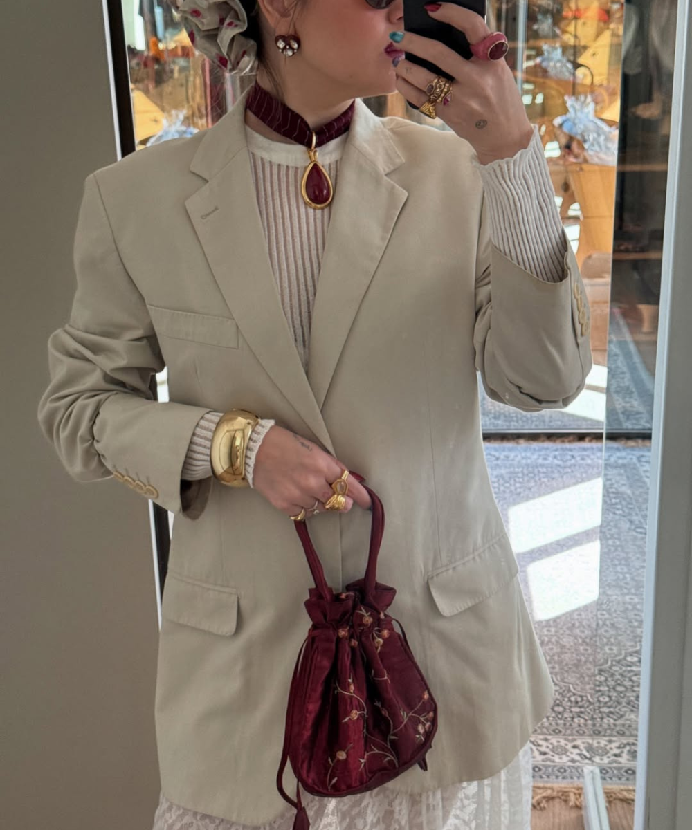 Modelo posa com lenço com pingente vinho, blazer bege e tricô canelado, em visual elegante e acolhedor.