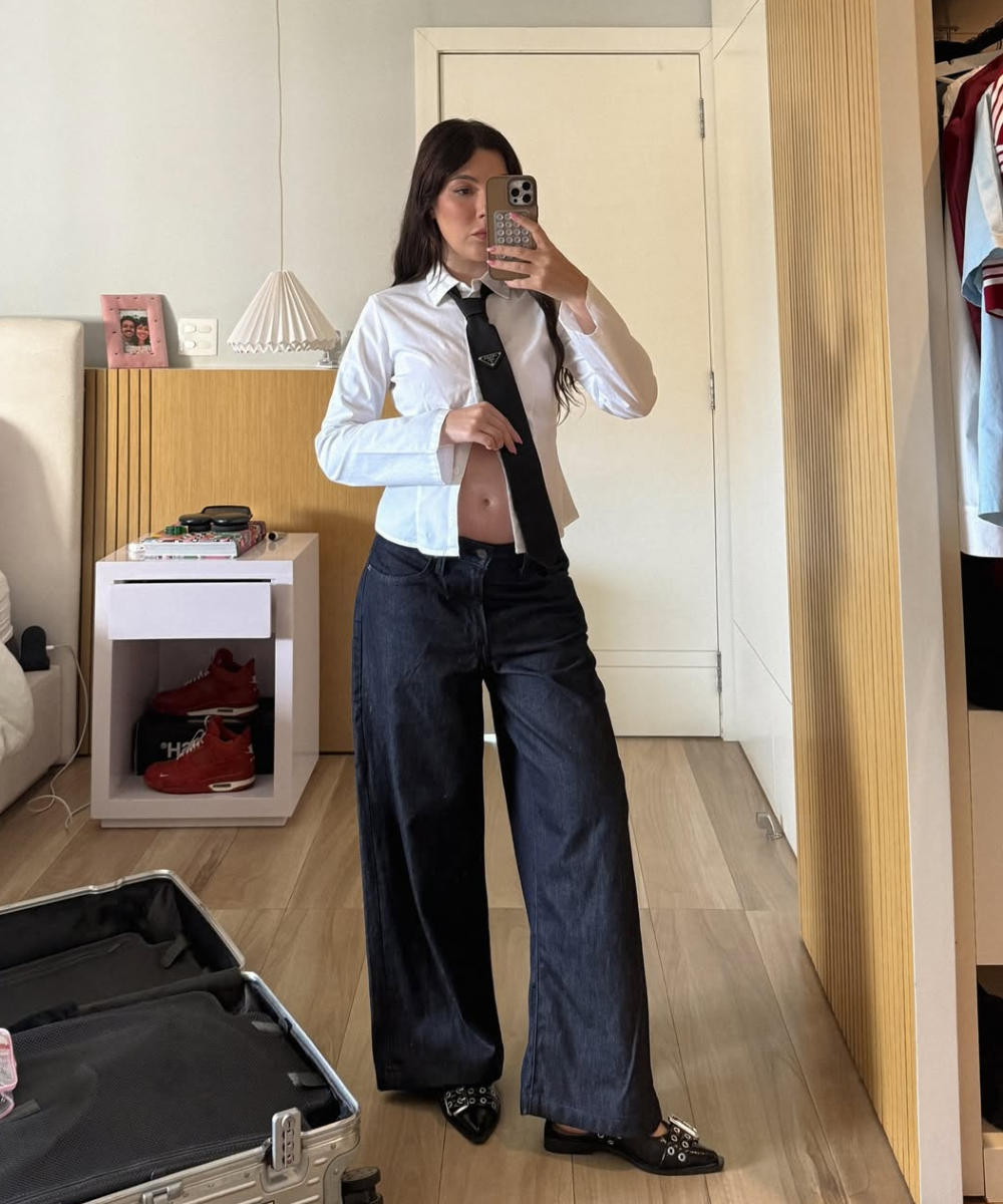 Looks de mulheres grávidas com modelo posa de camisa branca, gravata preta e calça ampla jeans em quarto neutro elegante