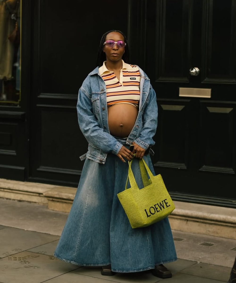 Looks de grávidas com modelo posa de jaqueta e saia jeans amplas, polo listrada cropped e bolsa verde. Texto: LOEWE