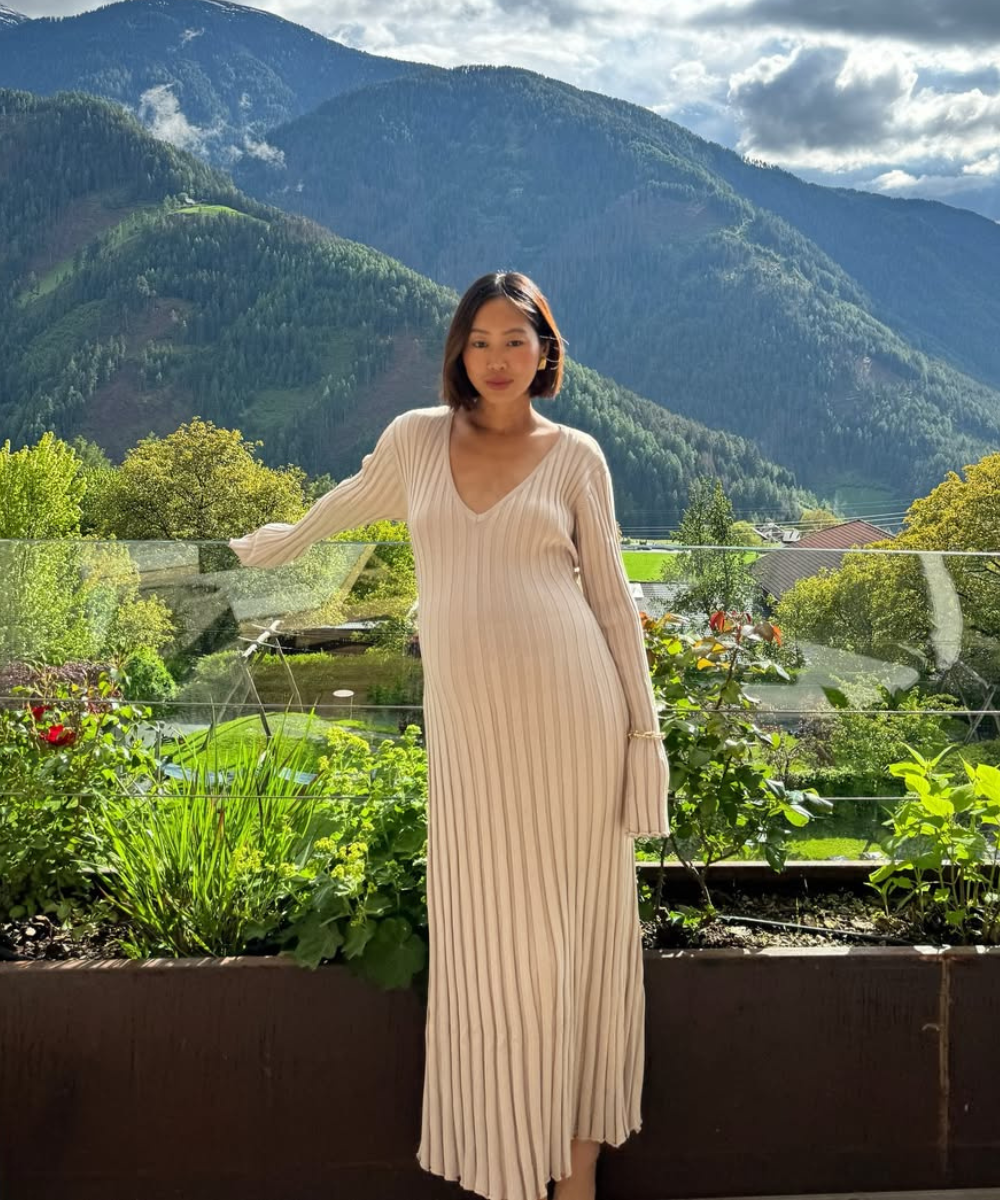 Looks de trabalho para usar durante a gravidez com vestido canelado bege de manga longa; modelo posa serena na varanda.