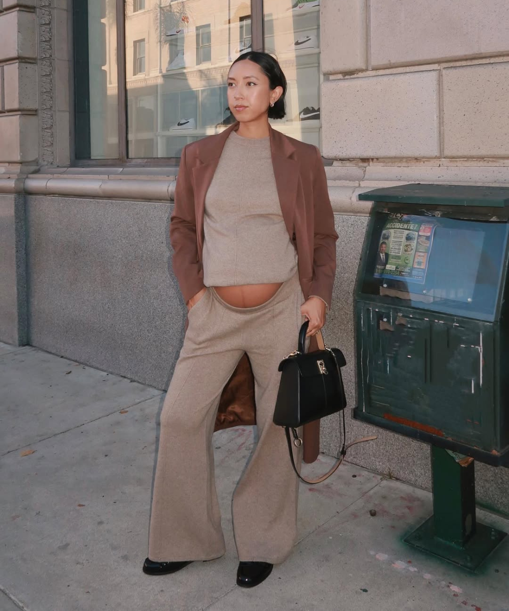Looks de trabalho para usar durante a gravidez com blazer marrom, malha bege e calça ampla; modelo posa elegante na rua.