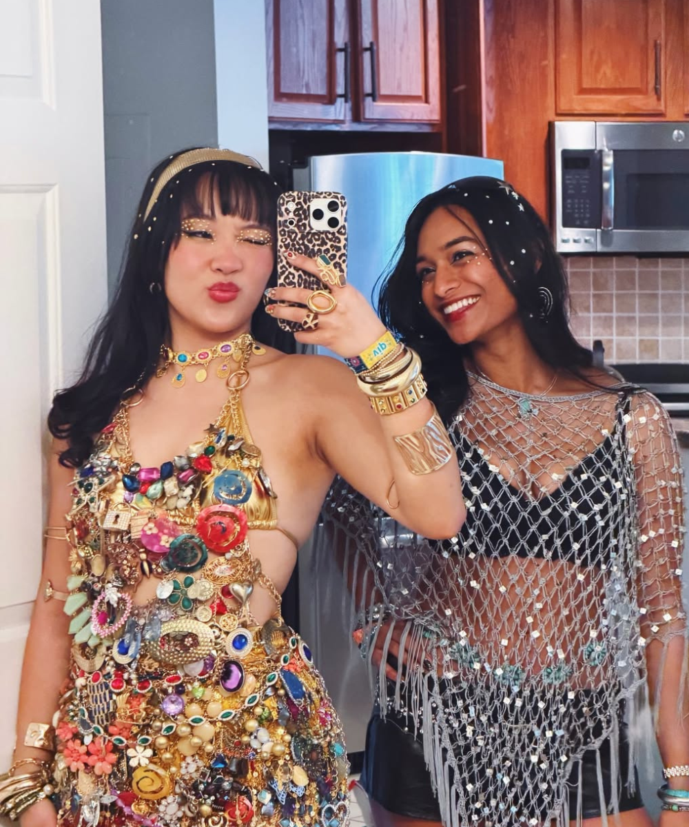 Strass no cabelo destaca duas mulheres posando no espelho com looks brilhantes, dourado maximalista e tela prateada, clima