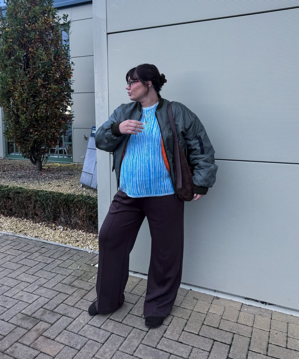 Looks de trabalho para usar durante a gravidez: modelo posa com bomber verde, blusa azul e calça ampla marrom em clima