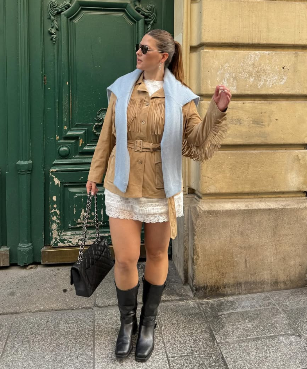 Looks com franja: modelo posa com jaqueta bege acinturada, vestido rendado branco, botas pretas e echarpe azul clara elegante