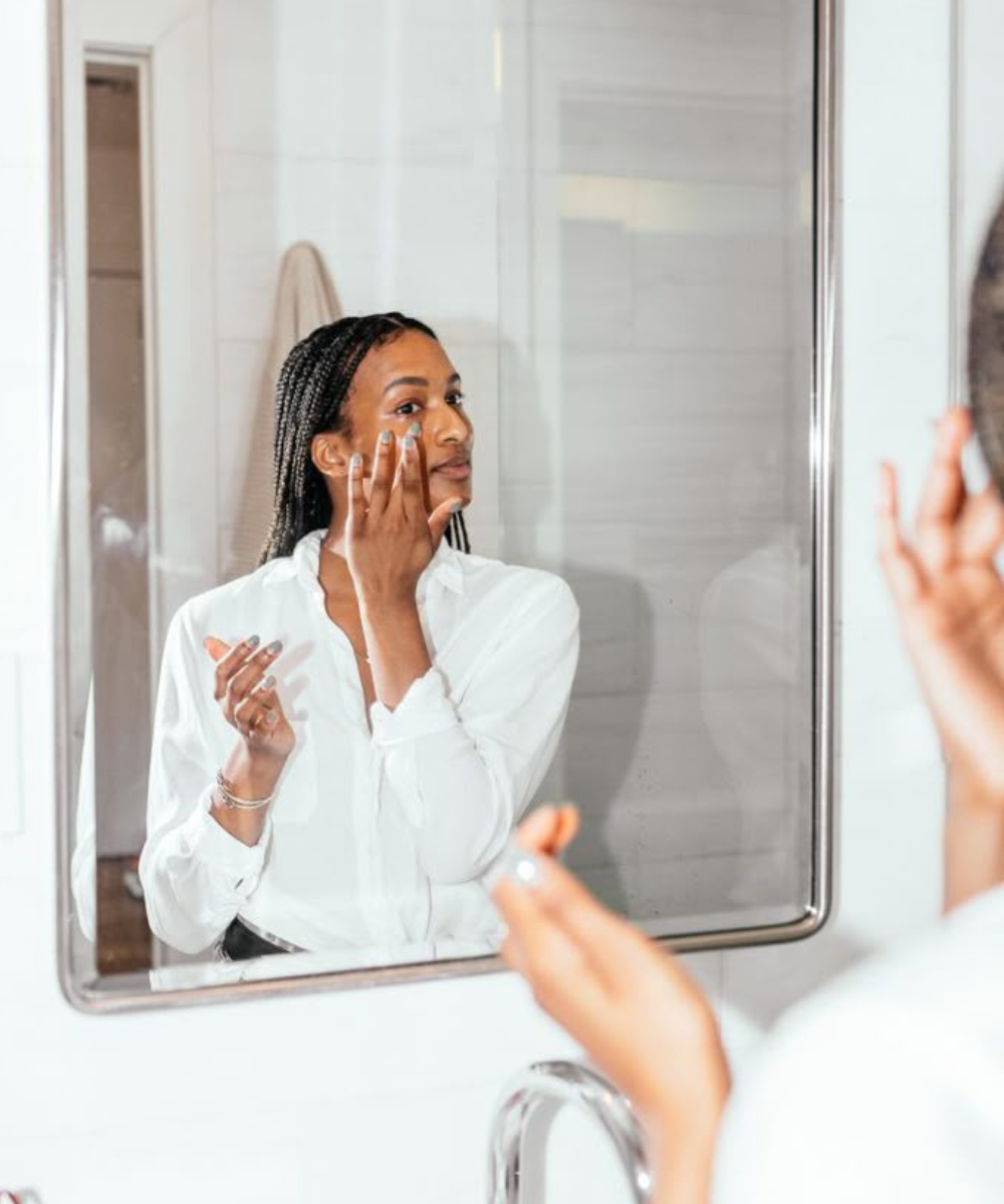 Modelo posa no espelho com camisa branca e aplica corretivo tem que ser mais claro que a base em clima leve no banheiro.