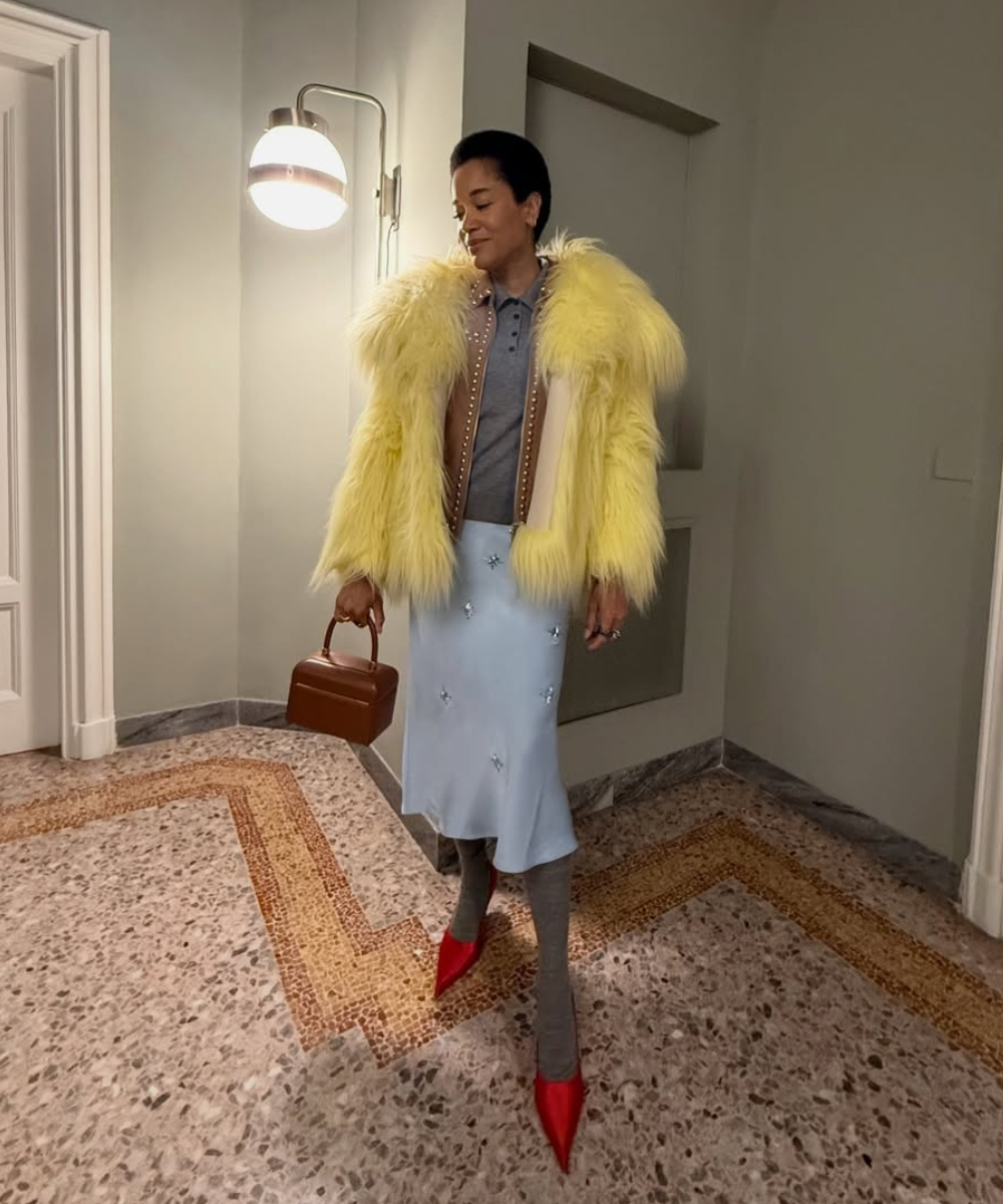 Modelo posa com sapatos de cetim vermelhos, casaco felpudo amarelo e saia azul-clara em hall elegante e acolhedor.