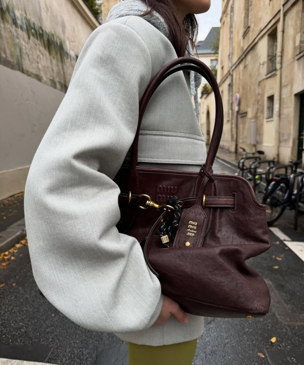 Modelo posa com casaco off-white e bolsa vinho em couro, uma das cores de bolsa mais chiques para o outono, em rua urbana