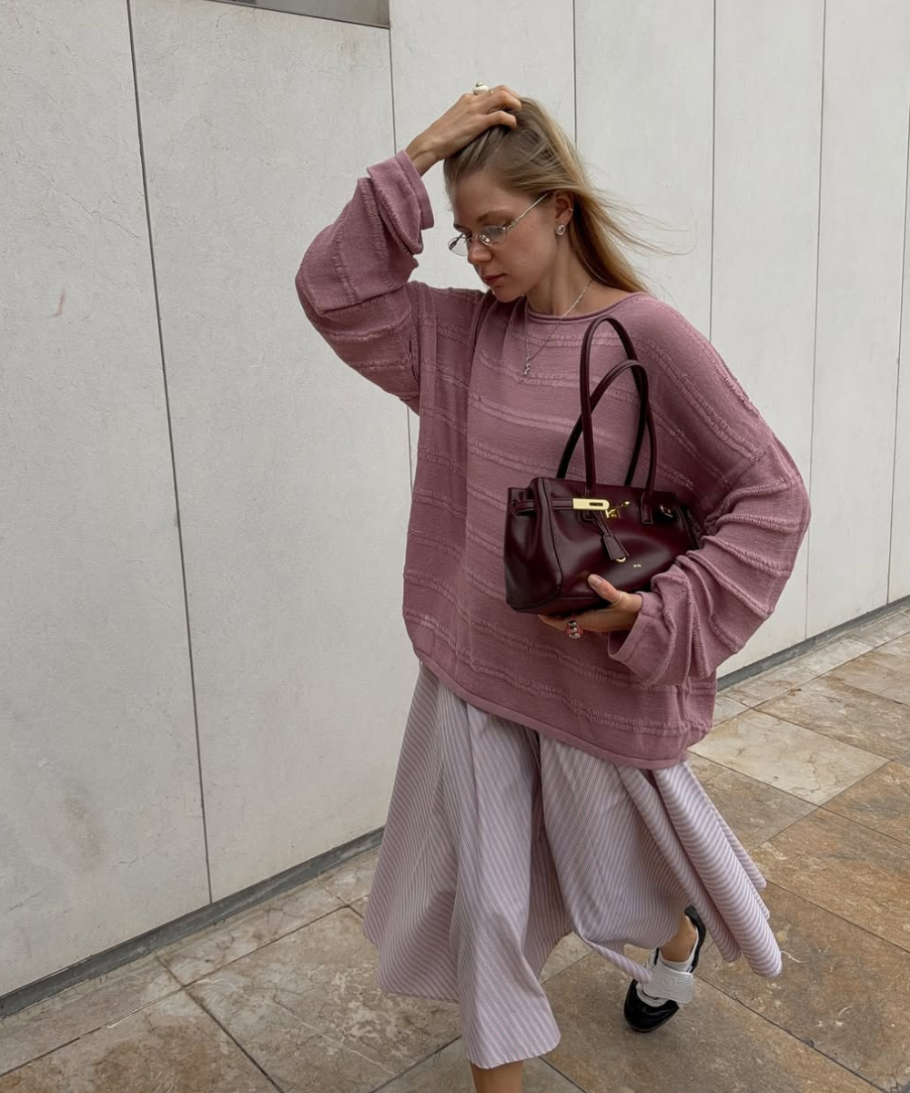 Modelo posa com tricô malva e saia fluida listrada; bolsa vinho é uma das cores de bolsa mais chiques para o outono.