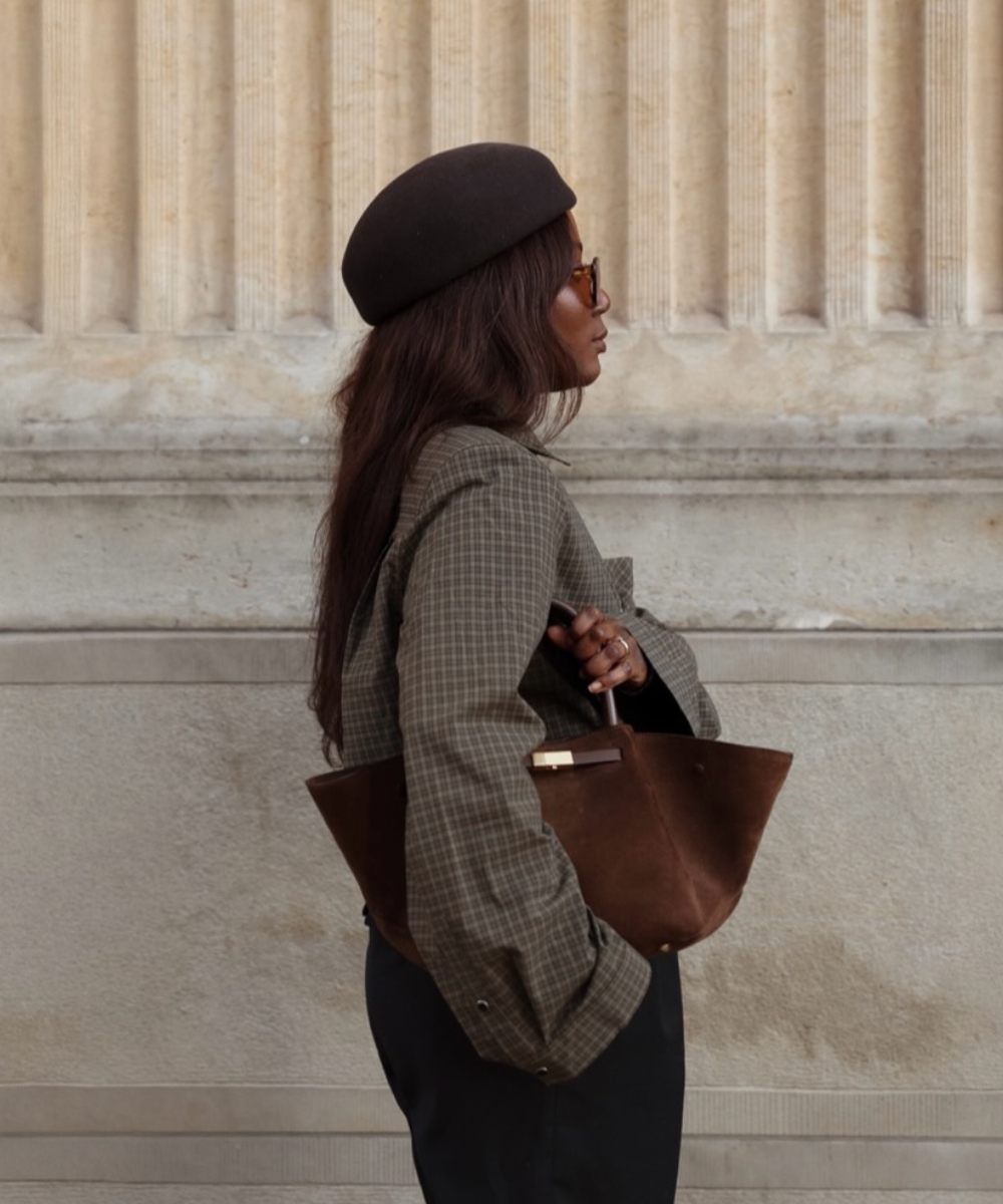 Modelo posa de perfil com boina e blazer xadrez; bolsa marrom de camurça destaca cores de bolsa mais chiques para o outono.