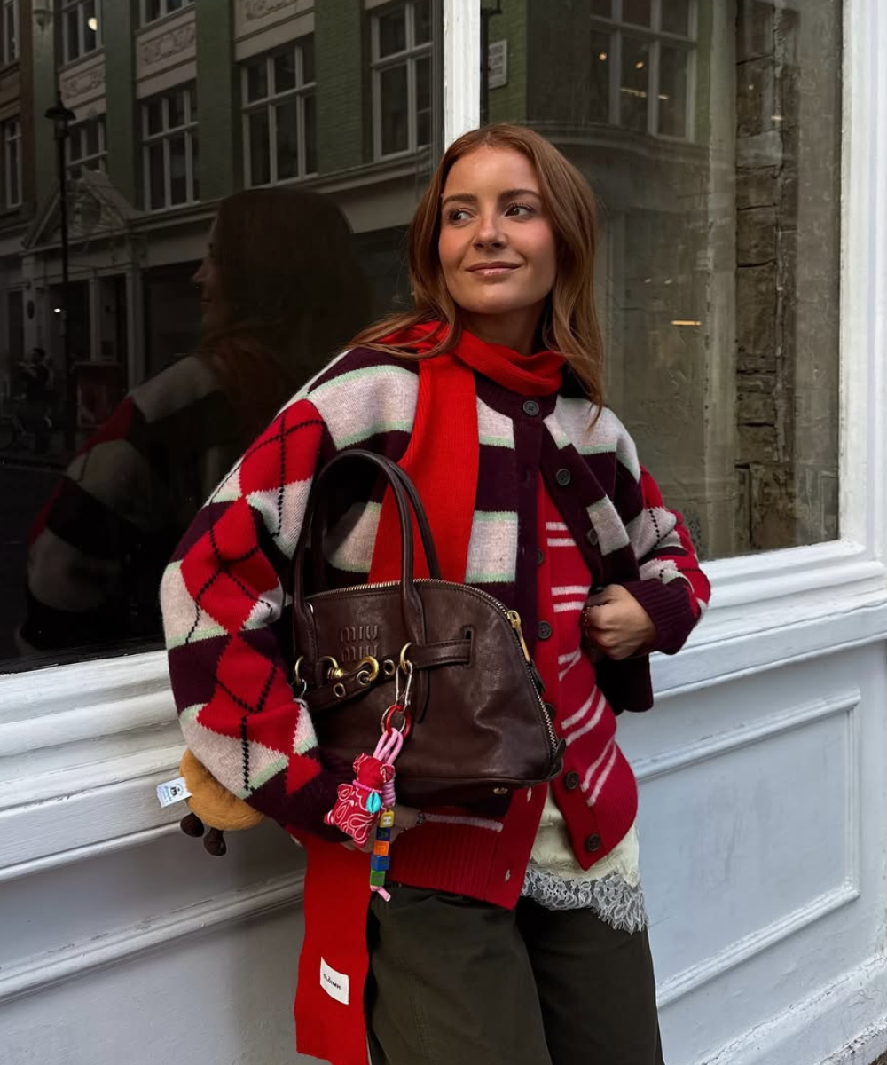 Modelo posa com bolsa marrom de couro, uma das cores de bolsa mais chiques para o outono, e tricô vermelho xadrez.