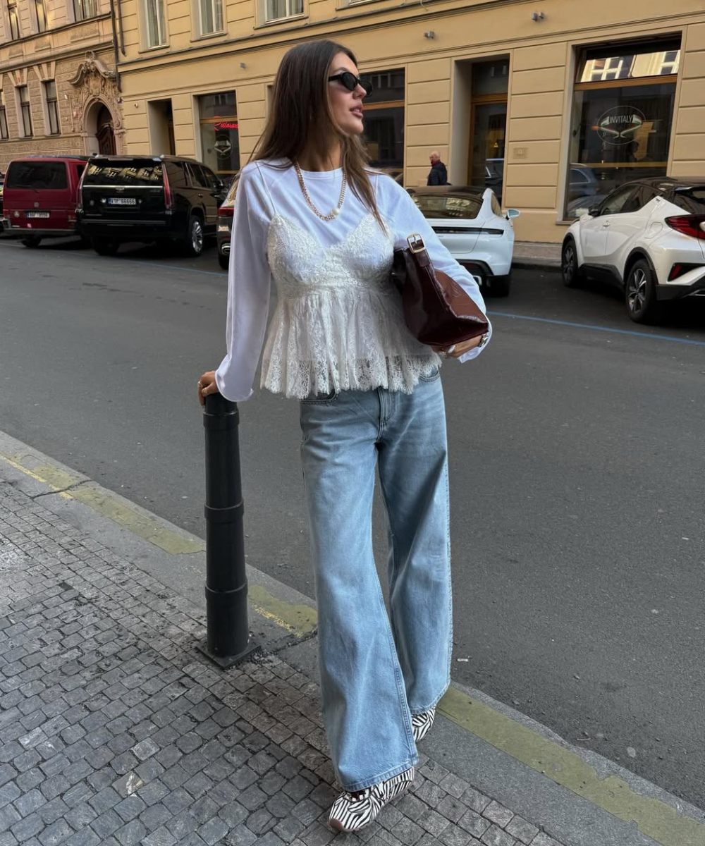 Modelo posa na rua com bolsa vinho, uma das cores de bolsa mais chiques para o outono, renda branca e jeans amplo.