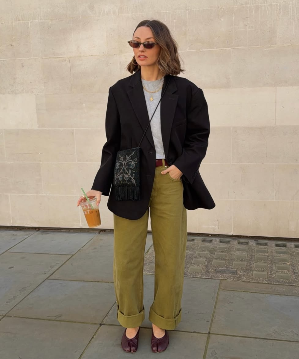 Modelo posa de blazer preto, calça oliva e bolsa preta bordada, uma das cores de bolsa mais chiques para o outono.