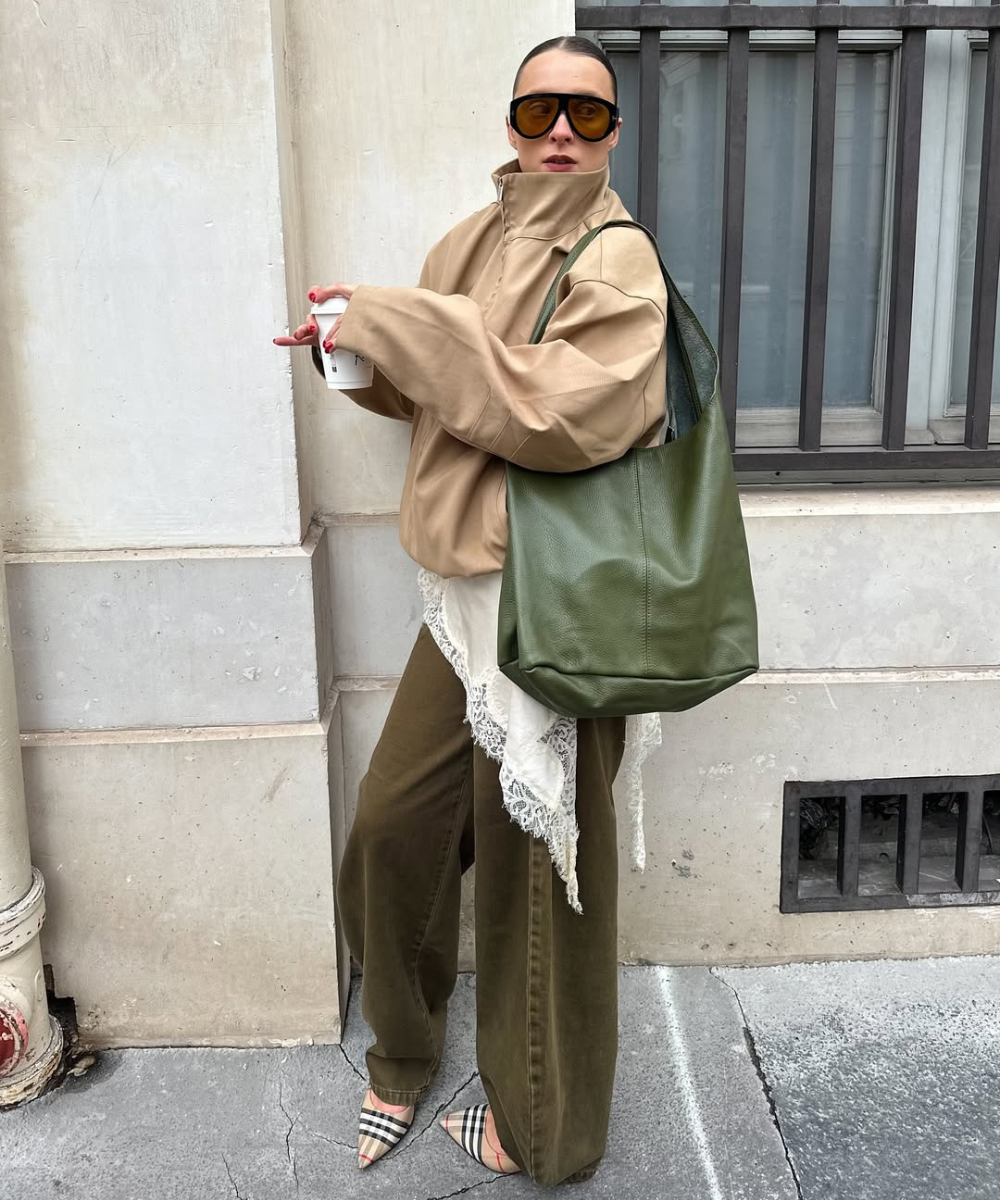 Modelo posa com jaqueta bege ampla, calça oliva e bolsa verde de couro, uma das cores de bolsa mais chiques para o outono.