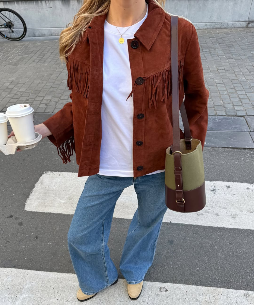 Cores de bolsa mais chiques para o outono: modelo posa com bucket verde e marrom, jaqueta suede caramelo e jeans amplo.