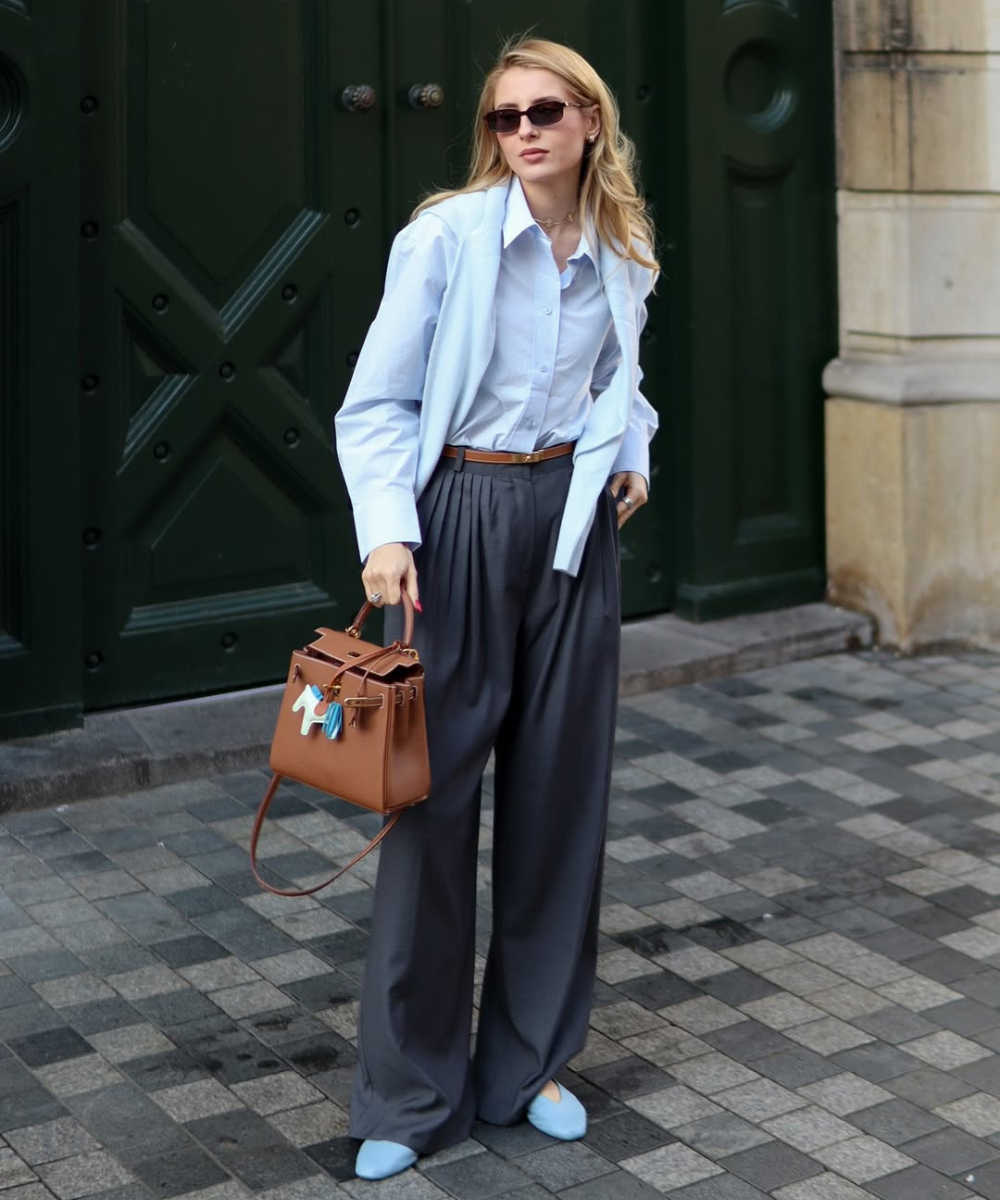 Modelo posa com camisa azul, calça ampla grafite e bolsa caramelo estruturada, uma das cores de bolsa mais chiques para o