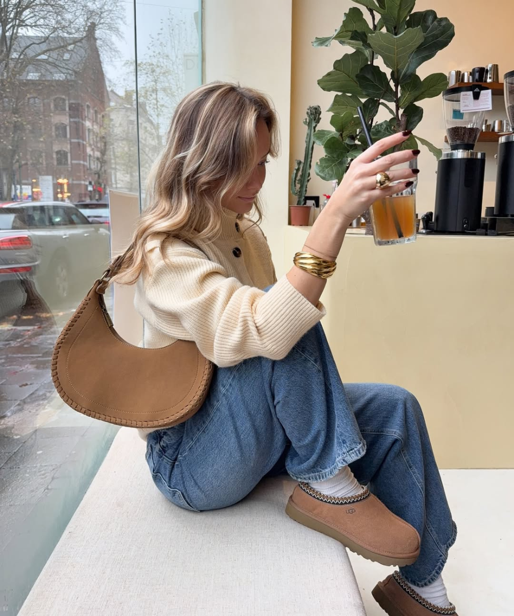 Modelo posa em café com bolsa caramelo, tricô creme e jeans amplo, look aconchegante com cores de bolsa mais chiques para o
