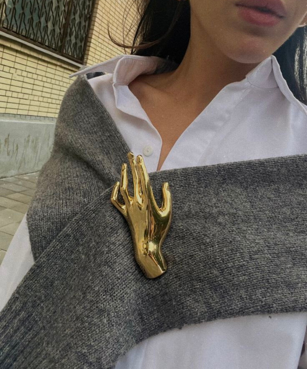 Acessórios para o outono em look minimalista com camisa branca, tricô cinza e broche dourado de mão, clima elegante.