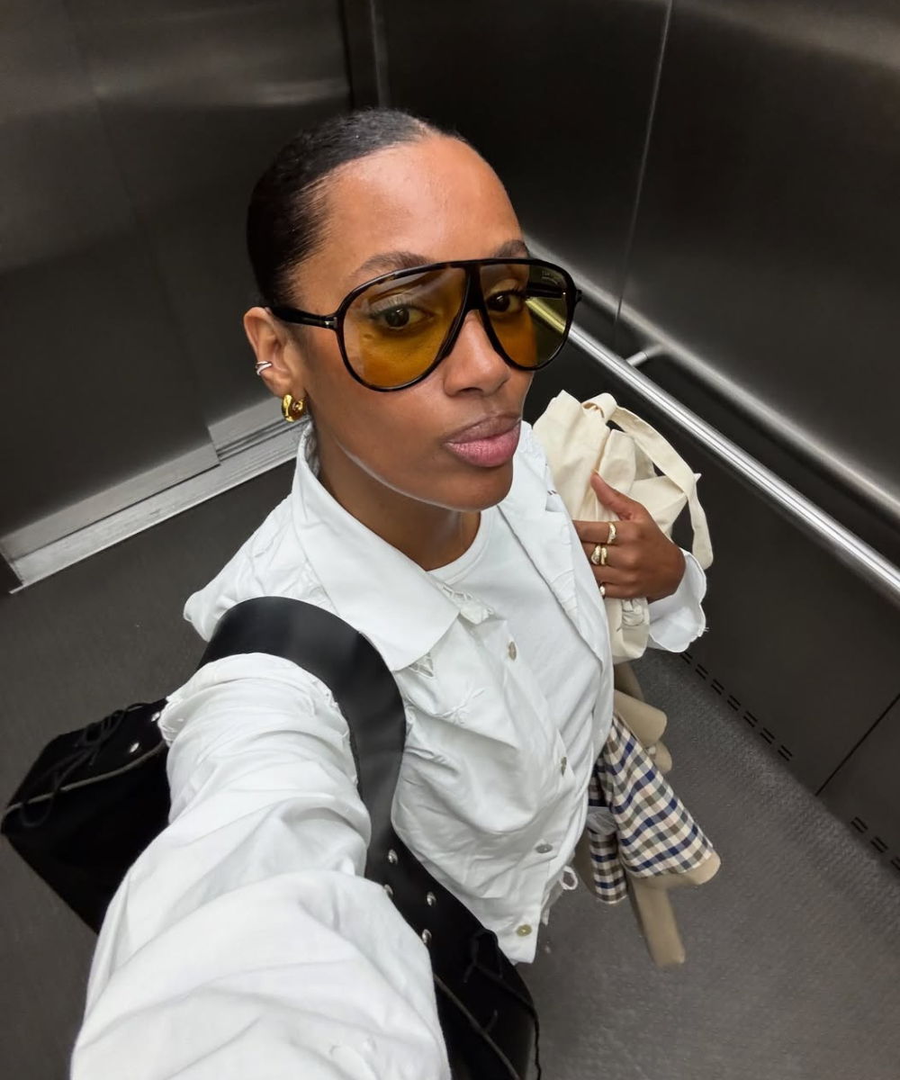 Modelo posa no elevador com acessórios para o outono: óculos âmbar, argolas douradas, camisa branca e bolsas neutras.