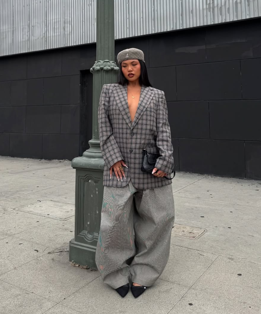 Acessórios para o outono: modelo posa de boina cinza, blazer xadrez e calça ampla em cenário urbano sóbrio.