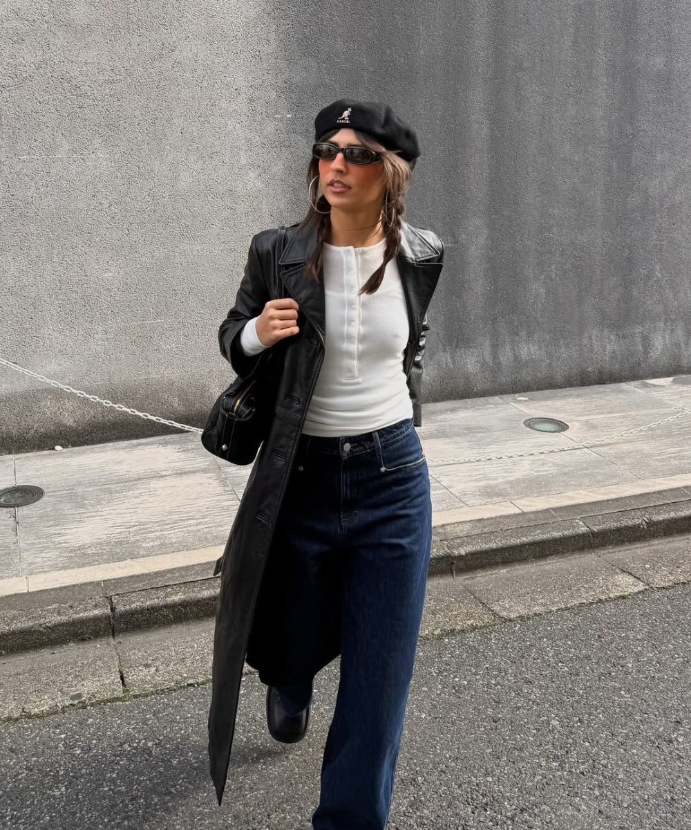 Modelo posa com acessórios para o outono: boina e óculos pretos, casaco de couro, jeans amplo e clima urbano elegante.