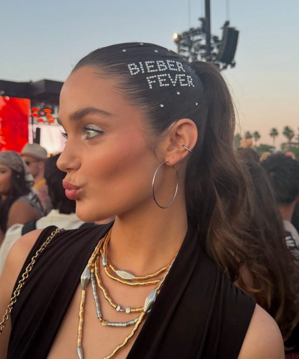 Modelo posa de perfil com strass no cabelo em rabo alto, vestido preto e argolas prateadas. Texto: BIEBER FEVER