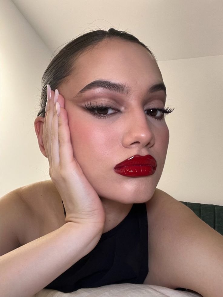Modelo posa com cores de batom vermelho vinil, top preto e maquiagem glow em close elegante e intenso.
