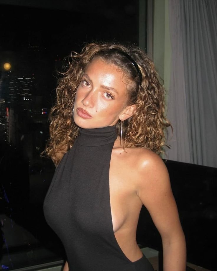 Modelo posa com vestido preto de gola alta e costas abertas, argolas e tiara, acessórios para o outono em clima sofisticado