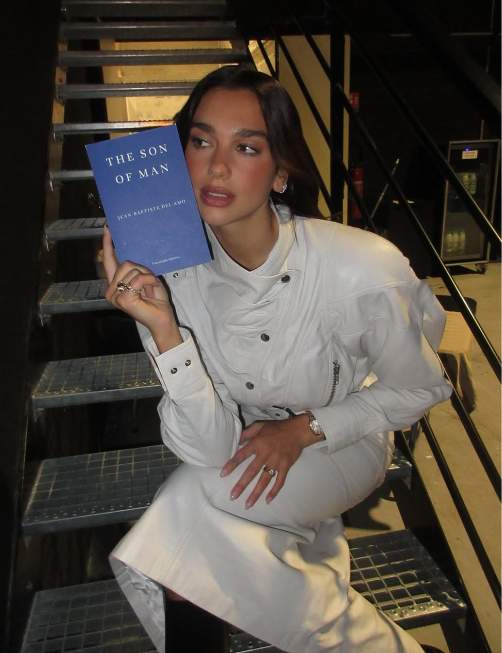 Dua Lipa posa de branco em look estruturado na escada industrial com livro azul.