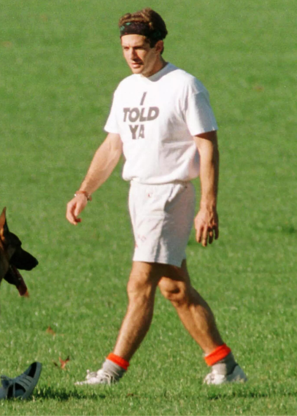 Modelo caminha no gramado com camiseta branca e shorts claros, visual esportivo retrô. Texto: I TOLD YA