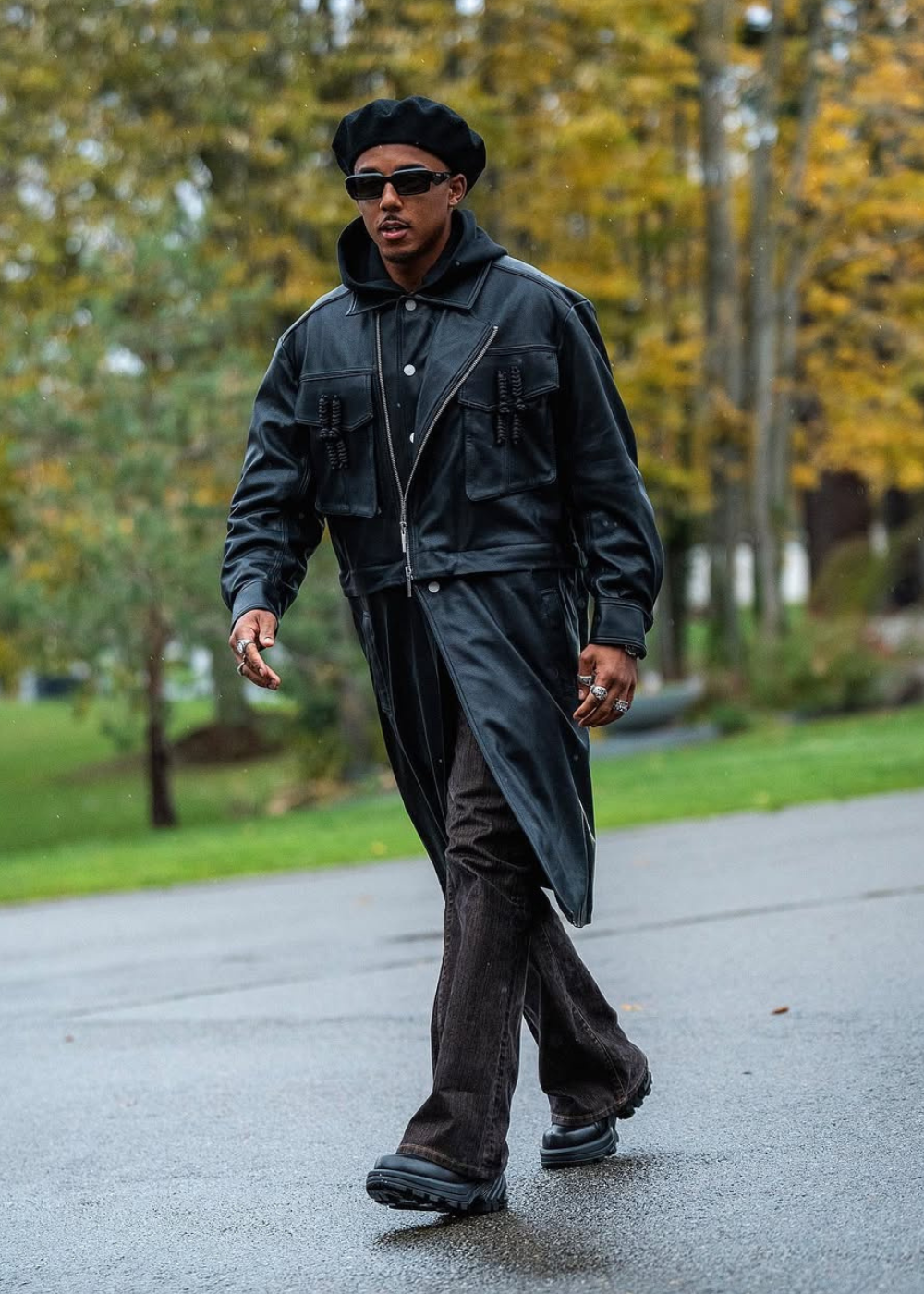 Jules Koundé caminha com atitude em look preto de couro e moletom, boina, óculos escuros e calça ampla em parque outonal.