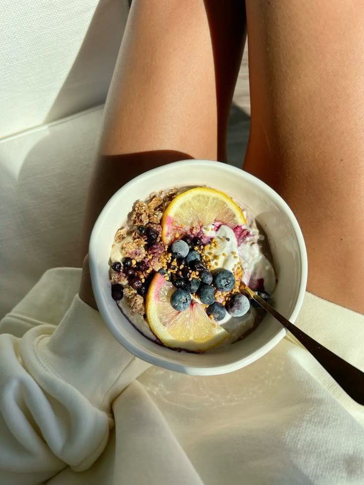 Receitas com iogurte em tigela branca com mirtilos, limão e granola sobre moletom claro criam clima leve e acolhedor