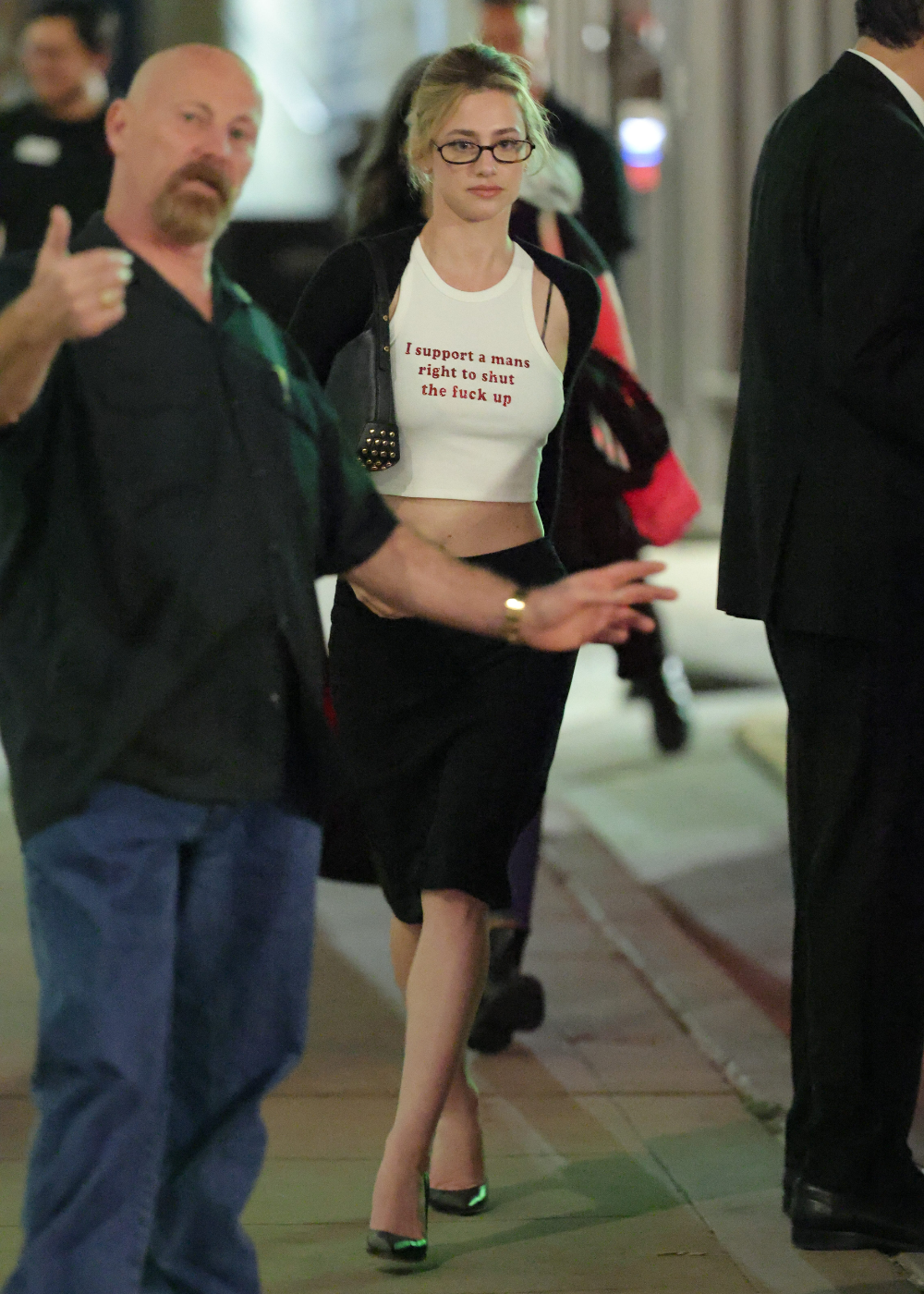 Modelo caminha com camisetas cropped branca, saia preta e cardigan. Texto: I support a mans right to shut the fuck up.