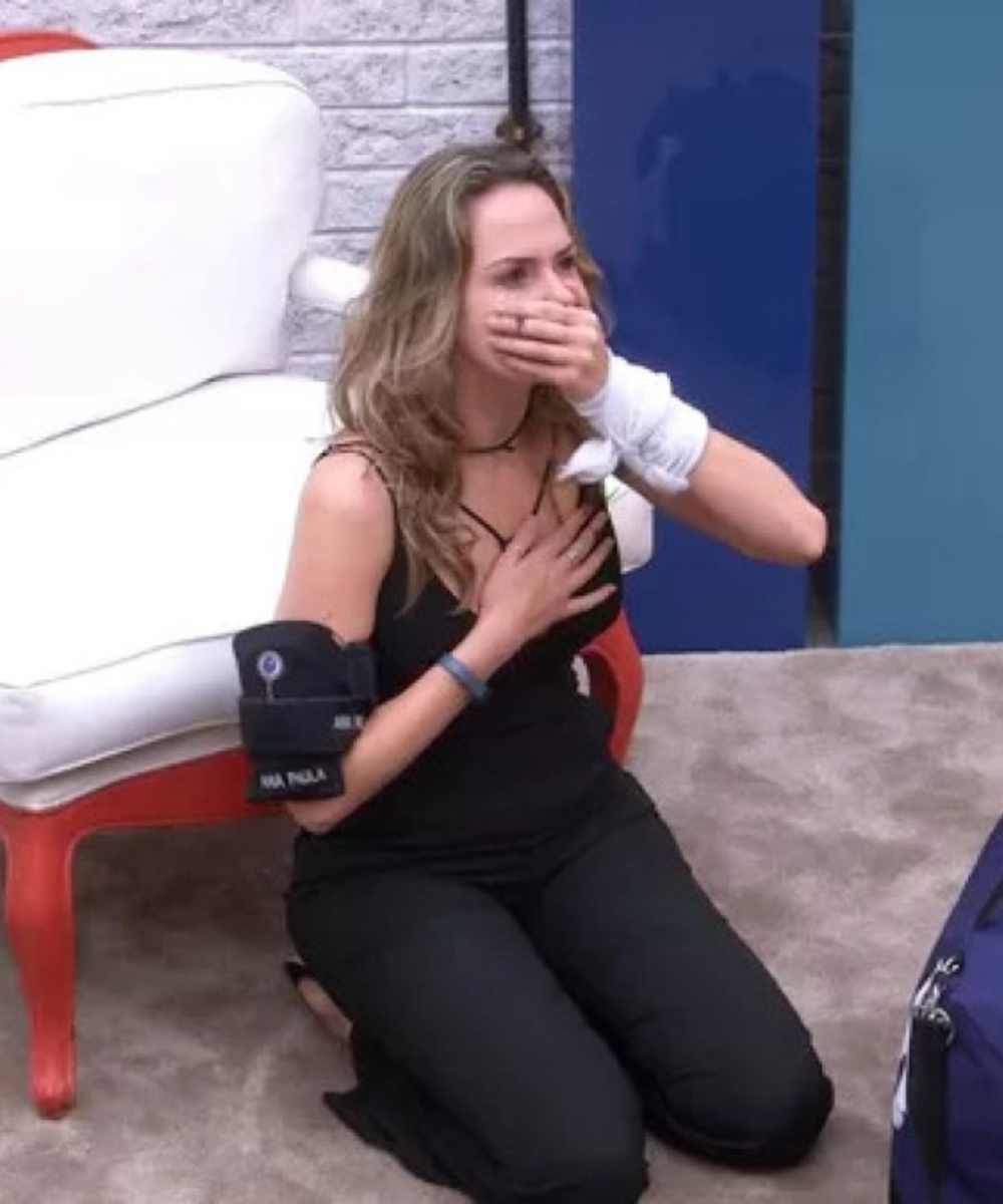 Look da Ana Paula na final do BBB 26 com macacão preto ajustado; ela ajoelha no tapete, emocionada, ao lado de poltrona