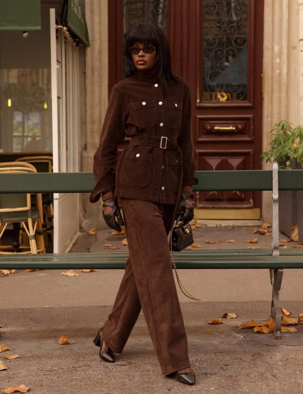 Looks com scarpin: modelo posa em conjunto marrom acinturado de camurça, luvas e bolsa preta, clima sofisticado.