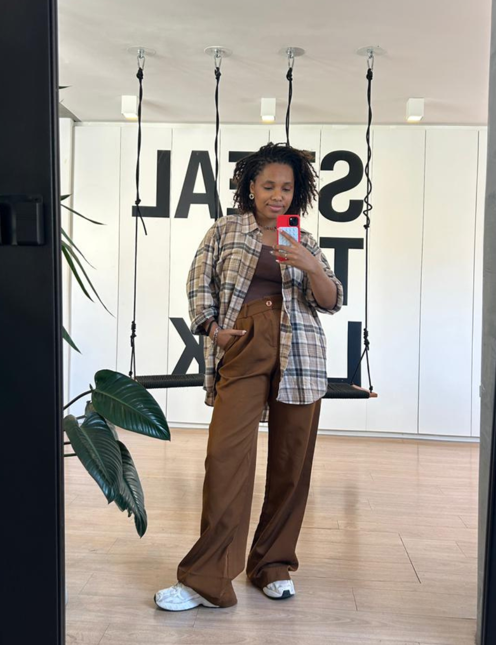 Looks de escritório com camisa xadrez ampla, regata e calça marrom fluida; modelo posa em clima casual.