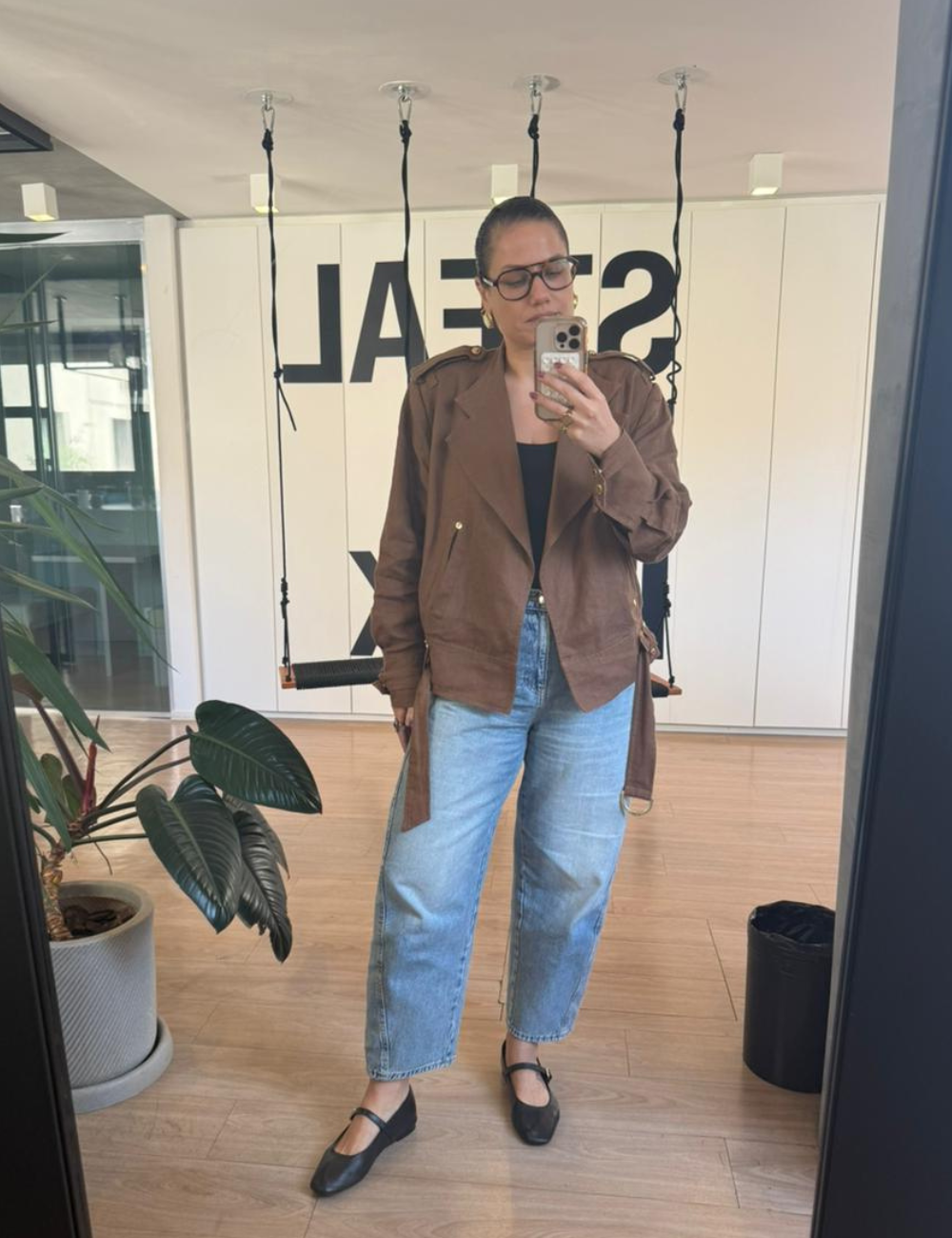 Looks de escritório com jaqueta marrom utilitária, jeans reto claro e sapatilha preta; modelo posa em clima casual elegante.