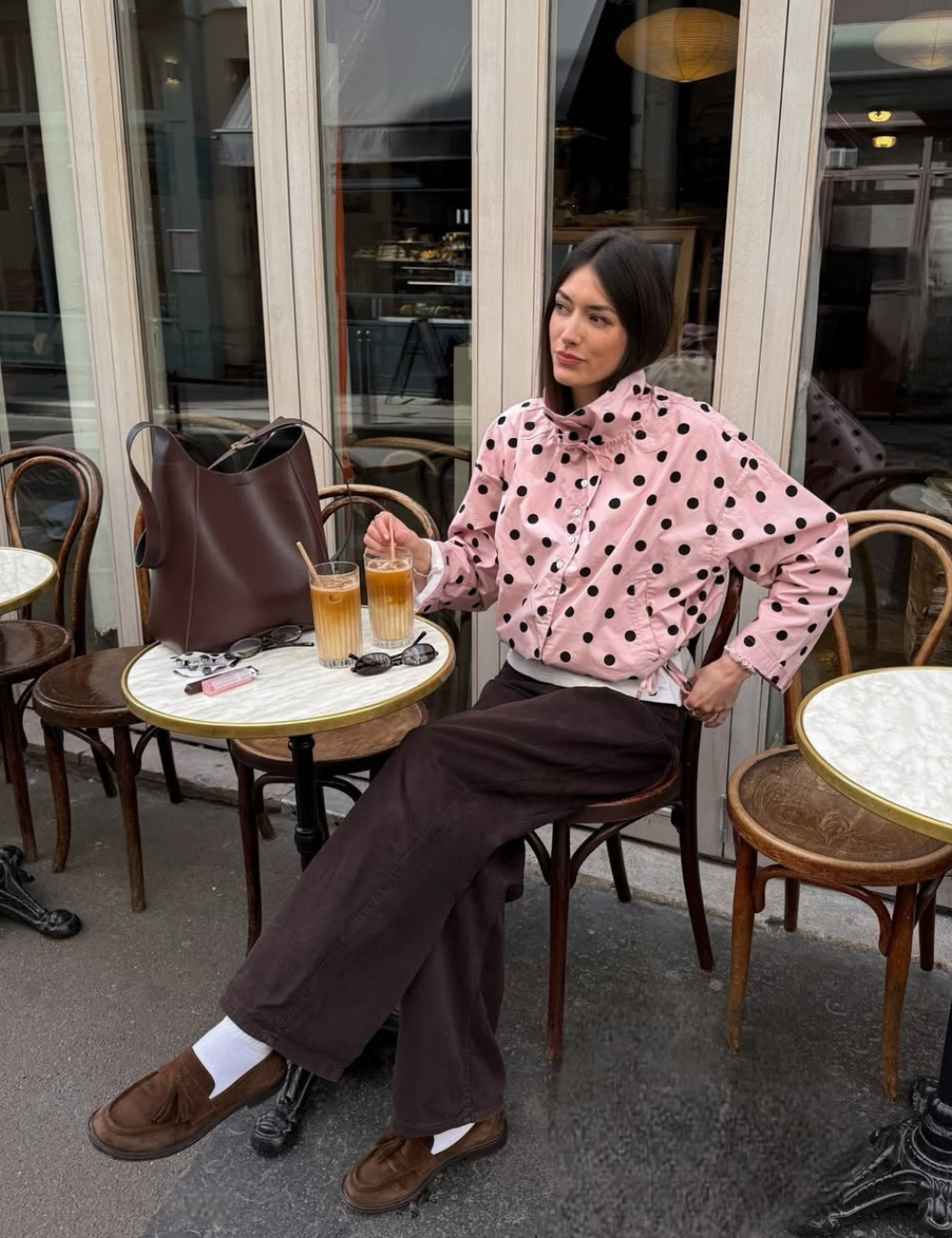 Modelo posa em café com mocassins femininos estilosos marrons, jaqueta rosa de poás, calça ampla marrom e clima elegante.