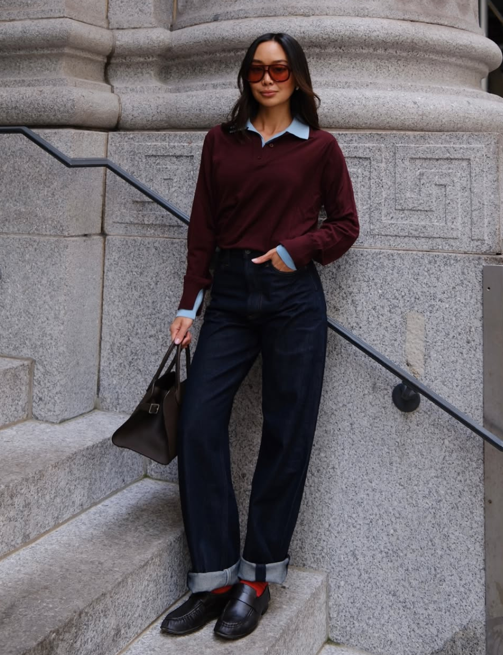 Mocassins femininos estilosos em couro preto com meia vermelha; modelo posa de jeans amplo, polo vinho e bolsa marrom.